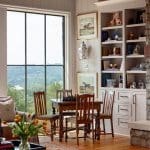 Dining table with chess set, wooden chairs, built-in bookshelves, and large window with view