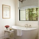 Freestanding bathtub with chrome fixtures, next to a small table with flowers.
