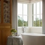 Bathroom with freestanding tub, wood cabinetry, and floral ottoman.