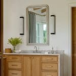 Bathroom vanity with light wood cabinets, marble countertop, and silver framed mirror.