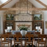 Dining room with stone fireplace, wood beams, and a large wooden table with upholstered chairs.