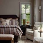 Bedroom with striped bedding, upholstered bench, armchair, and patterned rug.