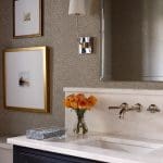 Bathroom vanity with marble countertop, dark blue cabinets, brass faucet, and framed art.