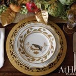 White plates with gold bird and leaf pattern on gold charger, silver cutlery, and festive