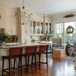 Cream kitchen with marble island, woven bar stools, and a decorated Christmas tree.