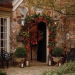 Stone house entrance with holiday garland, lanterns, and benches.