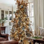 Flocked Christmas tree with gold and blue ornaments, lights, and ribbons. Leather armchair and