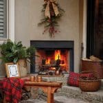 Outdoor fireplace with a roaring fire, decorated for winter with pine boughs, berries, and