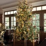 Christmas tree decorated with gold ornaments, ribbons, and birds in a wooden planter.