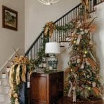 Staircase decorated for Christmas with garland, tree, and gold bows.