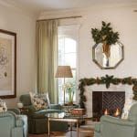 Living room with sage green chairs, marble fireplace, and gold chandelier.