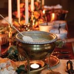 Brass fondue pot with bread on a skewer, lit candles, and oranges on a table