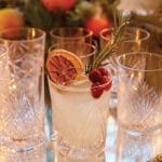 Crystal glasses with a cocktail garnished with dried orange, cranberries, and rosemary