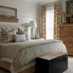 Bedroom with shiplap walls, patterned bedding, floral curtains, and wooden chest.