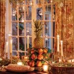 Dining table with a pineapple centerpiece, oranges, candles, and a cake.