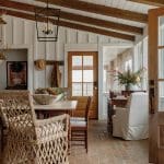 Dining area with wicker chairs, wood table, and brick floor. Rustic chandelier hangs overhead.