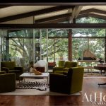 Living room with olive green velvet chairs, zebra rug, and large windows overlooking trees