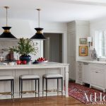 Kitchen island with pendant lights, marble countertop, and bar stools. White cabinets with brass