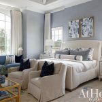 Bedroom with blue walls, white upholstered bed, blue sofa, and two cream armchairs.