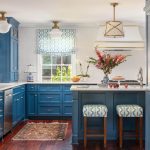 Blue kitchen with white herringbone tile backsplash, island with patterned stools, and brass
