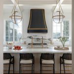 White kitchen with marble island, black range hood, and globe pendant lights.