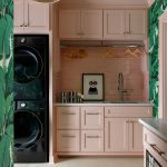 Pink laundry room with black washer/dryer, subway tile backsplash, and banana leaf wallpaper
