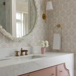 Bathroom vanity with pink cabinetry, marble countertop, brass fixtures, and floral wallpaper.