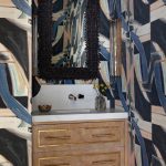 Powder room with abstract wallpaper, beaded mirror, marble vanity, and wood cabinetry