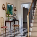 Entryway with black and white checkered floor, gold chair, console table, and staircase