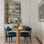 Dining area with teal velvet chairs, burl wood table, mirrored bar, and built-in cabinets.
