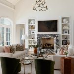 Living room with cream sofas, green armchairs, marble fireplace, and arched windows.