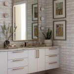 Bathroom vanity with white cabinets, marble countertop, brass hardware, and textured wallpaper.