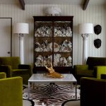 Living room with green velvet chairs, glass cabinet filled with coral, and zebra rug.