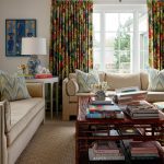 Living room with beige sofas, colorful floral curtains, and a rattan coffee table with books.