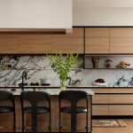 Modern kitchen with wood cabinetry, marble backsplash, and black bar stools.