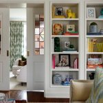Living room with built-in white bookshelves filled with books and decor, opening to a room with