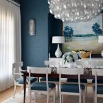 Dining room with blue grasscloth wallpaper, white chairs with blue cushions, and bubble chandelier.