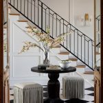 Entryway with black and white checkered floor, round table, and two fringe ottomans.