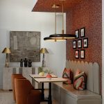 Dining nook with banquette seating, two tables, and velvet chairs. Red textured wall.