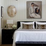 Bedroom with white paneled walls, black nightstand, leopard print pillows, and portrait painting.