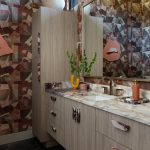 Bathroom vanity with wood cabinets, marble countertop, and geometric wallpaper.