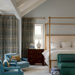 Bedroom with vaulted ceiling, patterned curtains, blue armchairs, and a four-poster bed.