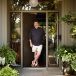Man in black shirt and shorts standing in doorway of home with plants