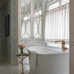 White clawfoot tub with brass faucet, mirrored cabinet, and floral wallpaper