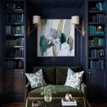 Living room with dark blue built-in bookshelves, green velvet sofa, abstract art, and glass coffee