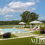Infinity pool with lounge chairs and umbrellas overlooking a lake and trees