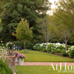 Lush garden with white hydrangeas, manicured lawn, brick path, and trees.