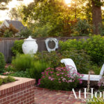 Garden with white urns, pink flowers, and a white chaise lounge.
