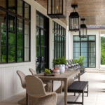 Covered patio with wood ceiling, black framed windows, and wicker dining set.