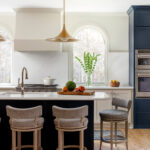 Navy blue kitchen island with leopard print bar stools, white quartz countertops, and brass pendant